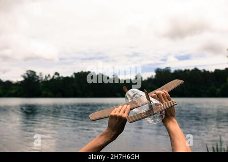 Les mains des enfants jouent avec un avion construit avec des matériaux recyclés (bois, bouteilles en PVC, carton) Banque D'Images