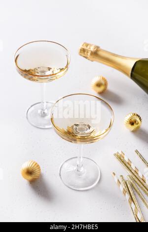 Champagne du nouvel an en verres et bouteille, boules dorées de Noël sur fond blanc.Composition verticale.Gros plan. Banque D'Images