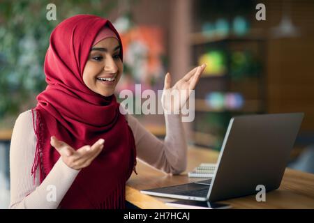 Gaie musulmane dans hijab ayant chat vidéo, à l'aide d'un ordinateur portable Banque D'Images