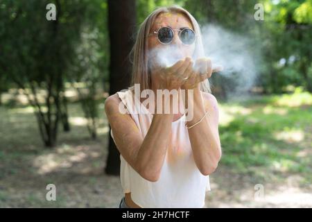 Une fille au Festival des couleurs de Holi souffle la poudre de ses mains avec de la peinture multicolore.Bonne femme à Color Fest.Concept de célébration Holi Banque D'Images