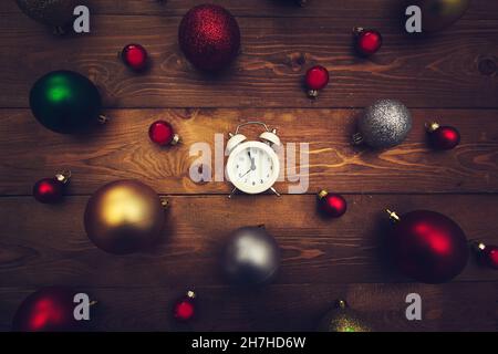 Réveil avec boules de Noël multicolores et minuit sur fond de bois.Arrière-plan de Noël sombre. Banque D'Images