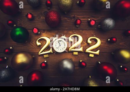 Bougies sous la forme de numéros 2022, réveil montrant minuit, boules de noël multicolores sur un fond en bois.Arrière-plan de Noël sombre. Banque D'Images