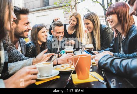 Des amis heureux qui parlent et s'amusent avec des téléphones mobiles intelligents au restaurant en buvant du cappuccino et du thé chaud - des jeunes ensemble à la cafétéria Banque D'Images