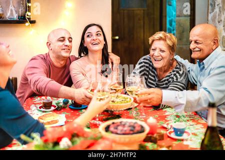 Groupe d'âge mixte toaster le vin blanc et s'amuser à la réunion des vacances d'hiver - concept de célébration du dîner avec des amis adultes heureux Banque D'Images