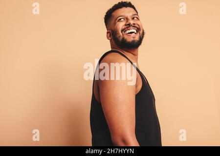 Homme barbu regardant loin avec un sourire sur son visage dans un studio.Un jeune homme heureux debout seul sur fond de studio.Corps positif homme sentiment c Banque D'Images