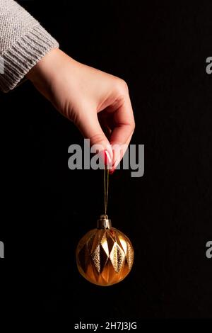 Chandail tricoté gris main féminine avec boule de Noël dorée et belle manucure - ongles rouges sur fond noir.Soins des ongles et de la peau confluent Banque D'Images