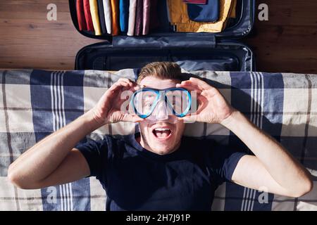 Portrait fou de jeune homme heureux lors de l'emballage de la valise et de la planification de voyage aventure. Banque D'Images