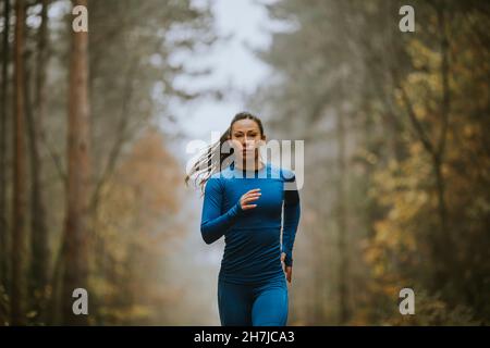 Jeune femme en costume bleu de course vers la caméra sur le sentier forestier à l'automne Banque D'Images