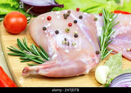 Viande de lapin rose cru non cuite avec romarin vert et légumes frais sur fond de planche à découper en bois clair. Banque D'Images