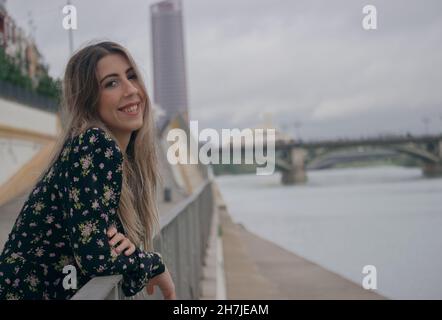 Une jeune fille touristique souriant directement à l'appareil photo lors d'un voyage en Europe et le pont Triana en arrière-plan.Voyager pendant le virus corona 2021-2022. Banque D'Images