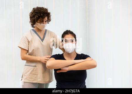 Une femme enceinte portant un masque facial faisant des exercices avec ses bras devant elle avec l'aide d'un physiothérapeute. Banque D'Images