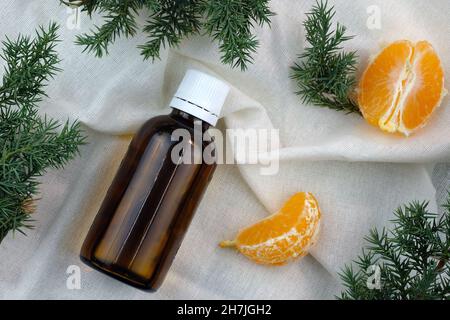 Une bouteille en verre brun avec un couvercle blanc sur un fond de tissu de lin.Huile cosmétique pour grains de mandarine, vue de dessus.Brindilles et huile de sapin.Santé et beauté co Banque D'Images