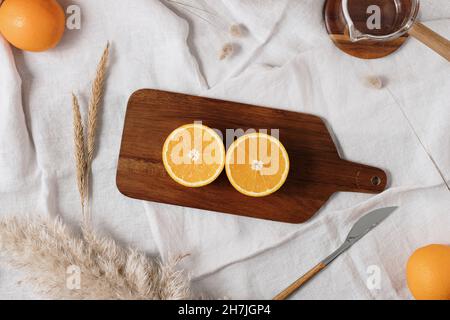 Deux demi-oranges sur une planche à découper en bois marron entourée d'un couteau, d'une tasse à verser et de fleurs séchées et d'oranges entières.Idée de petit déjeuner sain. Banque D'Images