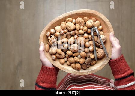 Une femme tenant un bol en bois de noix de Noël traditionnelles mélangées, toujours dans leurs coquilles, avec un casse-noix en métal traditionnel Banque D'Images
