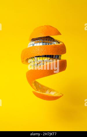 zeste d'orange autour d'une boule de miroir disco, flottant sur fond jaune Banque D'Images