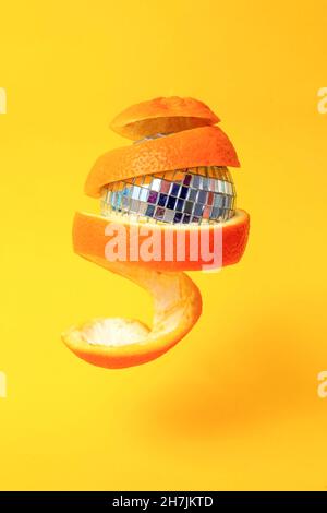 zeste d'orange autour d'une boule de miroir disco, flottant sur fond jaune Banque D'Images