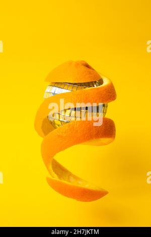 zeste d'orange autour d'une boule de miroir disco, flottant sur fond jaune Banque D'Images