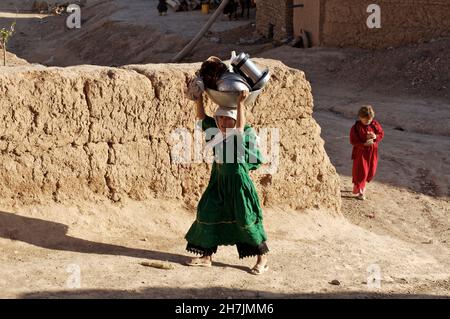 Basgul, 6 ans, une fille ethnique Hazara, retourne à la maison avec des articles de cuisine lavés, d'un ruisseau.Le ruisseau, traversant le village de Zargaran, en centre Banque D'Images