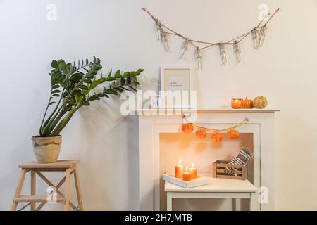 Cadre avec affiche « Happy Halloween ».Usine de Zamioculcas en pot d'argile sur tabouret.Le garland de squelettes est suspendu au mur.Guirlande de citrouilles en plastique suspendue Banque D'Images