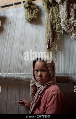 Zahra, 9 ans, une fille de la communauté ethnique Hazara, se tient devant un métier à tisser traditionnel, chez elle.Elle va à l'école, mais dépense le reste d'elle Banque D'Images