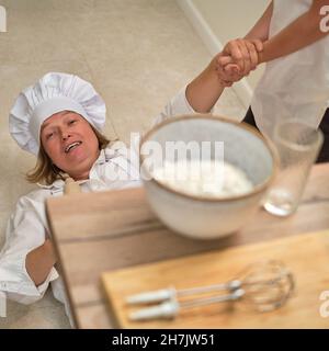 Maman et son fils drôles se détendent dans la cuisine après la cuisson. Une femme fatiguée et un garçon sont allongés sur le sol de la cuisine Banque D'Images