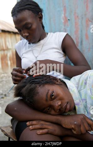 Une fille brase les cheveux d’une autre personne, à l’extérieur d’une habitation dans cite ?Soleil, l'un des quartiers les plus pauvres de Port-au-Prince, Haïti.Beaucoup de maisons et d'autres str Banque D'Images