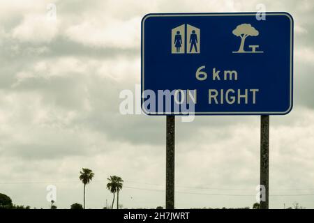 Toilettes et aire de repos devant le panneau droit sur la route contre un ciel nuageux par temps humide et pluvieux Banque D'Images