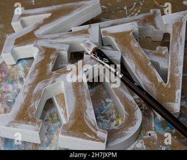 Diverses lettres non finies et non peintes en MDF sur une table d'atelier avec un pinceau Banque D'Images