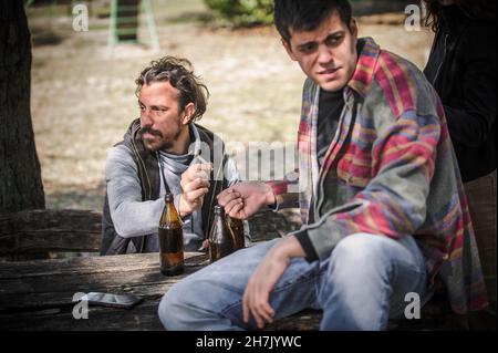 Les jeunes amis gardent la montre, regardent autour et essayent de cacher pendant que donne de la main à la main les uns les autres joint ganja dans le parc public en plein air.Fumer du cannabis ma Banque D'Images