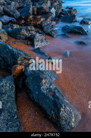 paysage marin abstrait de rochers côtiers sur une plage avec la mer tourbillonnant autour du rivage et de la côte, arrière-plan abstrait des rochers sur l'estran en basse lumière. Banque D'Images