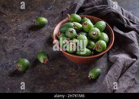 Fruits féijoa tropicaux mûrs dans un bol brun et sur la table de cuisine sur un fond sombre.Copier l'espace. Banque D'Images