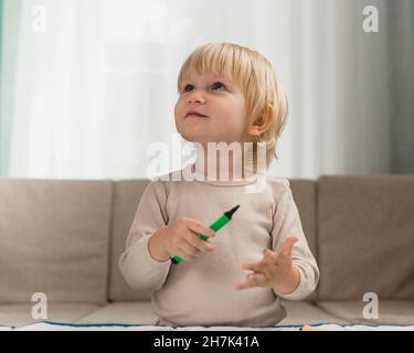Une petite fille gaie en pyjama à la maison dessine rêveur sur la table avec un stylo-feutre vert d'eau pour enfants Banque D'Images