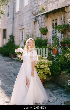 Une mariée avec un bouquet dans ses mains se tient sur une rue confortable de la vieille ville près d'un porche d'une maison Banque D'Images