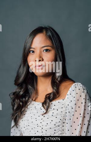 Jeune femme sérieuse avec cheveux noirs sur fond gris Banque D'Images
