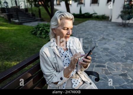 Femme âgée utilisant un téléphone portable assis sur un banc Banque D'Images