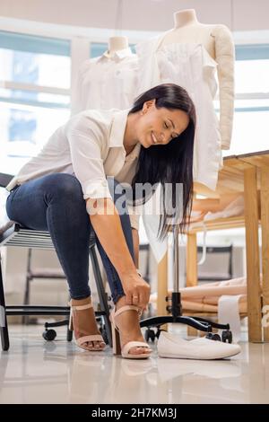 Belle femme vêtements de mode designer mettant sur des sandales après la journée de travail à l'atelier de couture Banque D'Images