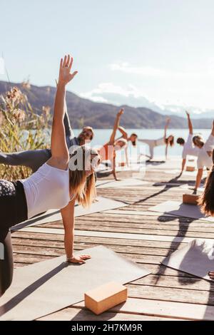 Hommes et femmes pratiquant le yoga sur des tapis d'exercice pendant la journée ensoleillée Banque D'Images