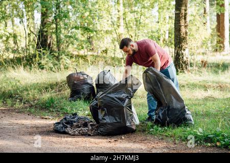 Activiste adulte moyen avec sacs à ordures dans la forêt Banque D'Images