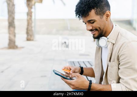 Homme souriant tenant le paiement par carte de crédit tout en utilisant un smartphone Banque D'Images