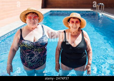 Des amies portant un chapeau de soleil debout dans la piscine pendant les vacances Banque D'Images