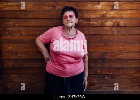 Femme âgée avec main sur la hanche debout devant un mur en bois Banque D'Images