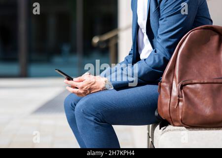 Homme professionnel utilisant un téléphone portable assis près d'un sac à dos Banque D'Images