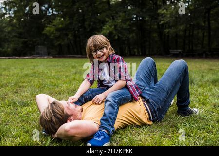 Garçon jouant avec le père allongé sur l'herbe dans le parc Banque D'Images