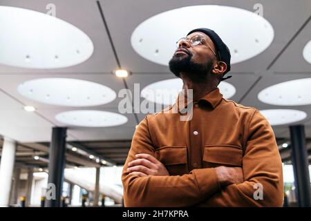 Homme barbu avec bras croisés regardant le plafond éclairé Banque D'Images