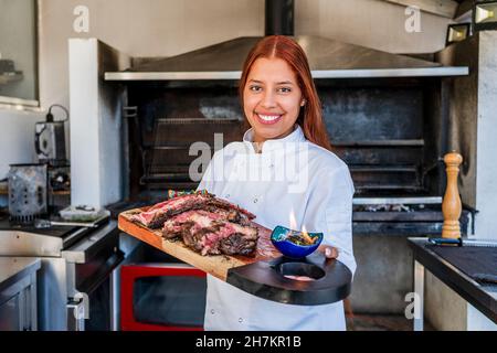 Femme souriante chef tenant une planche à découper dans la cuisine Banque D'Images