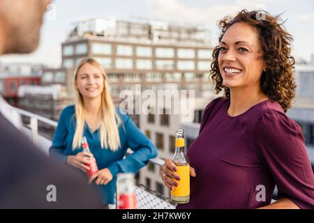 Femme d'affaires souriante prenant un verre avec ses collègues sur le toit Banque D'Images