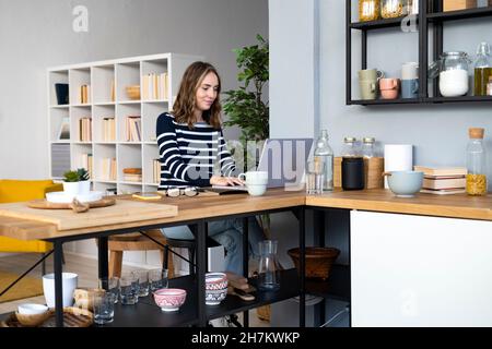 Jeune femme tenant un bol vu par une étagère dans la cuisine Banque D'Images