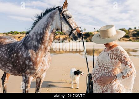 Femme enceinte à la main sur l'estomac debout à cheval à la plage Banque D'Images