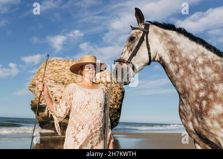 Femme enceinte avec cheval à la plage le jour ensoleillé Banque D'Images