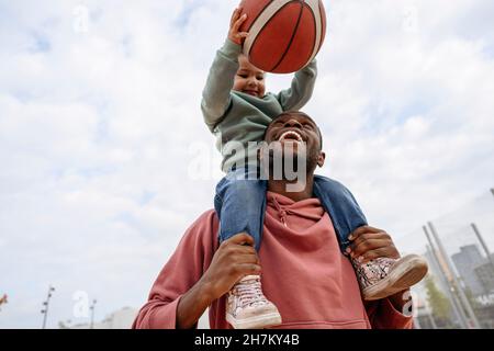 Père portant une fille ludique avec un ballon de basket sur les épaules Banque D'Images